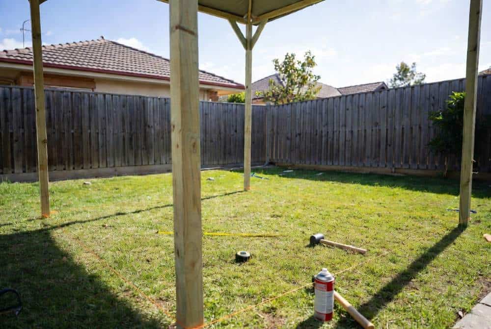 Marking Out Gazebo Site with String Lines – Australian Backyard Person marking out a square gazebo base with wooden stakes and bright string lines in an Australian backyard